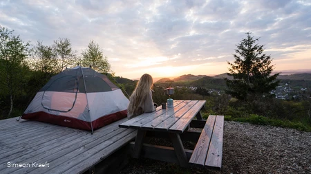 Eine Frau genießt den Sonnenaufgang am Trekkingplatz Talblick